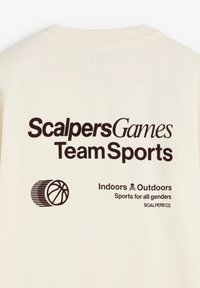 Sudadera color crema con texto gráfico negro: "ScalpersGames Team Sports," con un gráfico de baloncesto y neumático.