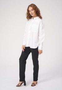 Hvid skjorte med knapper og brystlomme, parret med sorte skræddersyede bukser og højhælede sandaler med stropper. Glat stof, afslappet pasform.