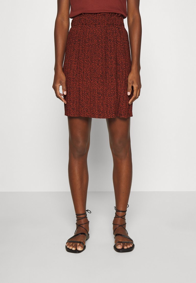 Jupe à motifs floraux rouges avec une taille élastique, longueur au-dessus du genou, plis superposés, associée à des sandales noires à lanières.