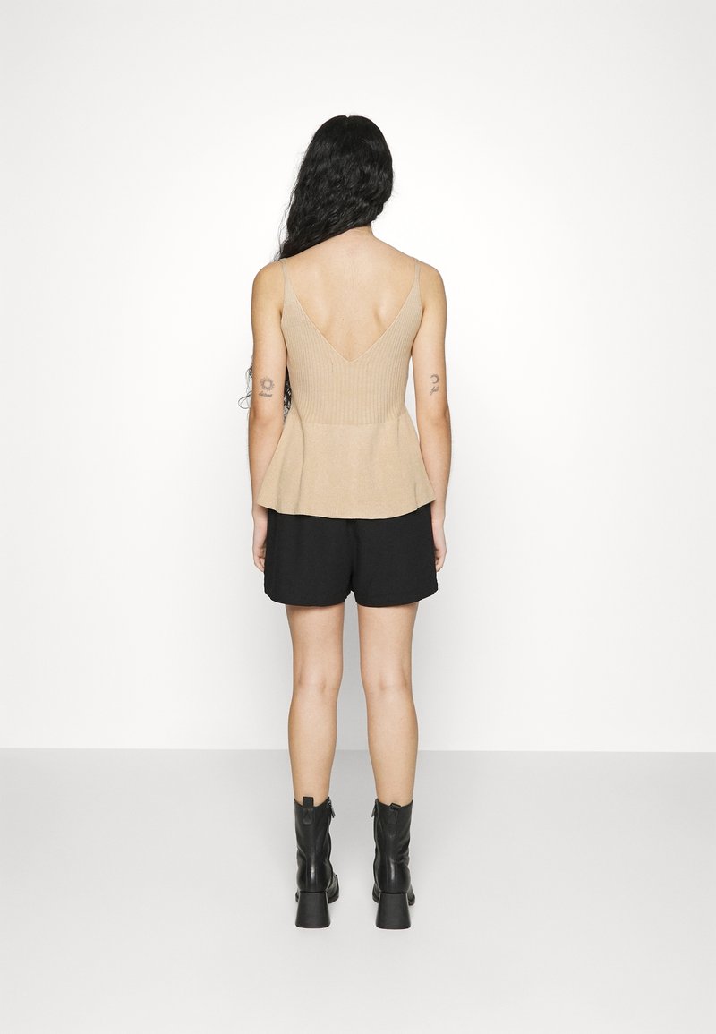 Beżowy prążkowany top na ramiączkach z głębokim dekoltem z tyłu, połączony z czarnymi szortami i czarnymi botkami na obcasie, wyeksponowany na białym tle.