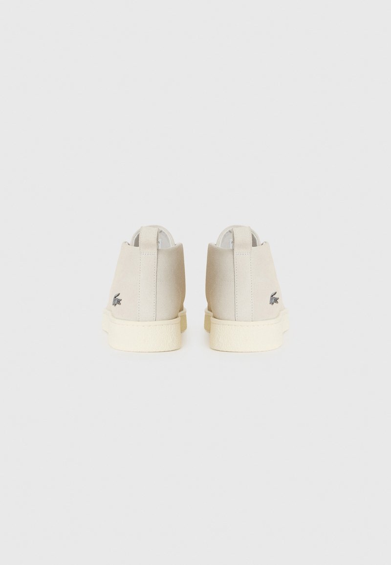 Bottines en suède beige avec des semelles en caoutchouc crème et de petits logos brodés sur le talon extérieur, vues de dos.
