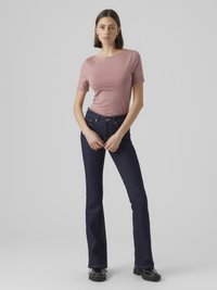 Ufjernede mørkeblå jeans kombinert med en tettsittende lyserosa T-skjorte. T-skjorten har korte ermer og et subtilt grafisk design på forsiden.
