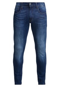 Mörkblå denimjeans med smal passform, markerat blekta områden på låren, fem fickor och en liten metalldetalj som knäppning.