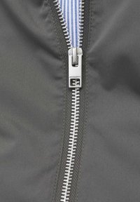 Gray jacket fabric featuring a metal zipper with alternating silver teeth and a blue-striped pull tab. Detail shows sturdy stitching alongside the zipper.