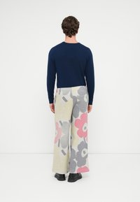 Dlhý rukáv námornícky sveter v kombinácii so svetlosivými nohavicami s veľkými kvetinovými vzormi v ružovej, šedej a žltej farbe. Pevné čierne topánky.