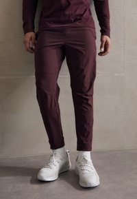 Bordo stiepļu bikses ar slim fit, ar gludu tekstūru un potītes garuma buķetēm, apvienotas ar baltām sporta kurpēm un zeķēm.