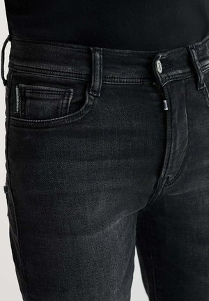Zwarte denim jeans hebben een klassieke snit met een rits als sluiting, vijf zakken en subtiele stiksels. De stof heeft een gladde textuur.