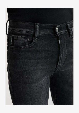 Zwarte denim jeans hebben een klassieke snit met een rits als sluiting, vijf zakken en subtiele stiksels. De stof heeft een gladde textuur.