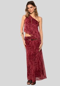 Vestido maxi en rojo intenso, con un diseño de un solo hombro, tejido transparente con un sutil estampado animal y un cinturón a juego con acentos circulares.