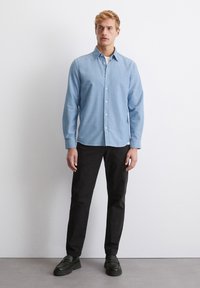 Light blue button-up shirt with long sleeves, a pointed collar, paired with black trousers and dark loafers. Simple and fitted design.