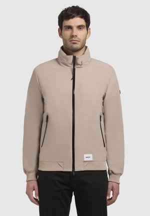 Beige jas met hoge kraag, ritssluiting aan de voorkant, twee zijzakken, elastische manchetten en een merketiket aan de zoom. Glad, mat aanvoelend.