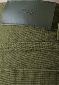 Oliegroen denimstof met subtiele textuur, voorzien van een leren label met de opdruk "7 For All Mankind" en gelijkmatig gestikte naden.