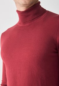 Pulover roșu cu guler înalt din țesătură netedă, cu un design ajustat și guler cu nervuri, văzut din umeri în sus.