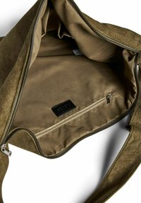 Olīvu zaļas auduma somas iek�špuse ar gludu tekstūru, ar rāvējslēdzēja kabatu un melnu etiķeti, kas izstrādāta izturībai un organizācijai.