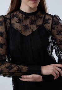 Black dress featuring sheer floral lace sleeves, a high neckline, and a fitted bodice. Delicate texture with layered fabric and patterned details.