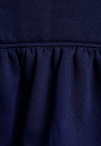 Marinblå stickad tyg med samlad volangdetalj vid fållen, som har en mjuk textur och jämn söm genom hela.