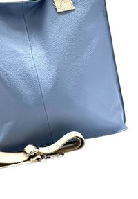 Blauwe leren draagtas met een gladde textuur, voorzien van een crèmekleurige stoffen schouderband en chroomkleurige hardware, gestructureerd ontwerp met verticale naden.