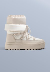 Bézs vízálló bokacsizma párnázott felsőrésszel, texturált fehér díszítéssel, rugalmas fűzőkkel és vastag, masszív talppal a jobb tapadás érdekében.