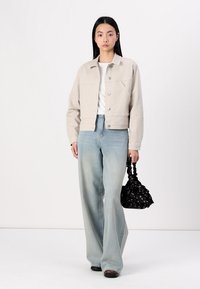 Veste cropped rayée beige avec poches avant, accompagnée de jeans bleus clairs à jambes larges. Sac noir avec une finition texturée.