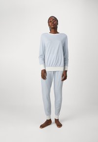 Hellblau gestreiftes Pyjama-Set aus weichem Stoff. Langärmliges Oberteil mit weißen Bündchen, dazu passende Hosen mit schmalen Bündchen und dezenten Streifen.