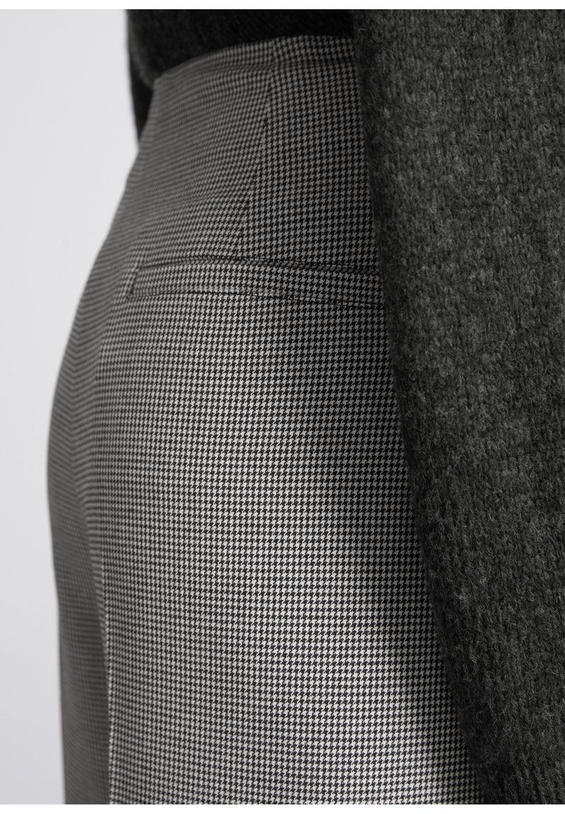 Maßgeschneiderte hochgeschnittene Hosen im schwarz-weißen Hahnentrittmuster. Eigenschaften sind eine glatte Textur und ein Rückentaschendetail.