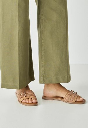 Barna színű fonott szandál három pánttal, lapos talppal és fafelületű talppal. Laza, olívazöld nadrággal viselve, laza stílust sugározva.