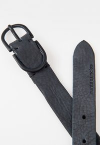 Zwarte leren riem met een gestructureerde afwerking, voorzien van een rechthoekige matte zwarte gesp en gegraveerde branding op de band.