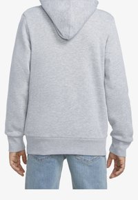 Felpa grigia chiara con cappuccio regolabile e polsini a costine. Tessuto morbido e vestibilità rilassata, abbinata a jeans in denim blu.