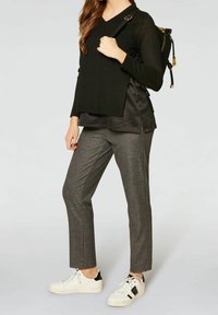 Pull noir à col en V superposé à un haut noir brillant, associé à un pantalon gris à carreaux et des baskets blanches avec des accents noirs. Sac à dos noir inclus.