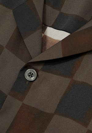 Brown and black checkered fabric with a textured finish, featuring a prominent round gray button at the collar.