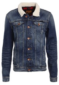 Blå denimjacka med en vit konstfårskinnskrage, som har två bröstfickor, bruna knappar och en lätt sliten textur.