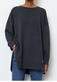 Tmavě šedá oversized mikina s kulatým výstřihem a spadlými rameny, s žebrovanými manžetami a bočními rozparky pro snadnější pohyb.