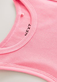 Ružová žebrovaná látka s okrúhlym výstrihom a detailmi švov. Obsahuje malú nálepku s čiernym nápisom "NEXT".