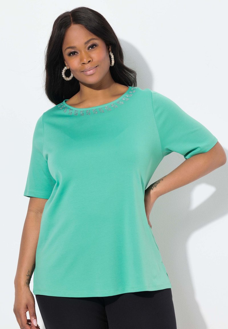 Tyrkysový top s krátkým rukávem vyrobený z měkké tkaniny, s kulatým výstřihem a dekorativními kovovými akcenty kolem límce.