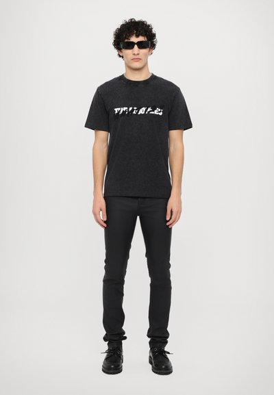 Zwarte korte mouw t-shirt met een versleten witte tekstafdruk, gecombineerd met zwarte slim-fit broek en zwarte veterschoenen.