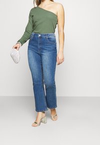 Green, long-sleeve, one-shoulder top; high-waisted, straight-leg blue jeans; silver heeled sandals; silver clutch purse.