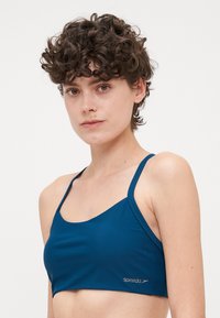 Blå bikinitopp med minimalistisk design, med tynne stropper og glatt tekstur. Stoffet er lett og elastisk. Speedo-merke til stede.