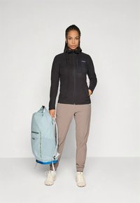 Mustast fliisist jope kapuutsiga, esikäepidemega ja rinnataskuga; hele sinine seljakott roheliste detailidega; beežid püksid; valged tennised.