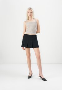 Striped halter top in cream and brown, paired with a black pleated mini skirt. Model wears black pointed-toe slingback heels.