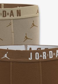 Boxers en coton marron et beige avec ceintures élastiques, présentant des motifs répétitifs du logo Jordan et des lettres contrastantes.