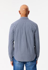 Camicia a maniche lunghe con bottoni, caratterizzata da un motivo a quadretti navy e azzurri, realizzata in cotone con colletto classico e orlo curvo.