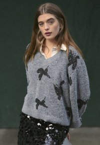 Maglione grigio con motivi di farfalle in paillettes nere, design a scollo a V, texture morbida; abbinato a una gonna con dettagli in paillettes nere.