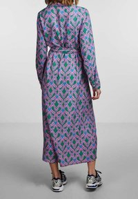 Långärmad, flerfärgad klänning med ett mönster i grönt, lila och rosa. Bärs med mörka sneakers och knyts i midjan. Slät tygstruktur.