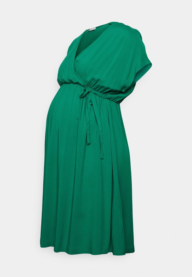 Robe de maternité verte à manches courtes, col en V et taille ajustable avec un lien, présentée sur un fond uni clair.
