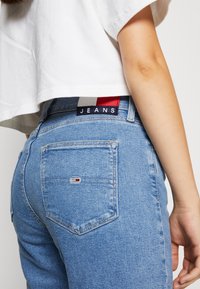 Jeans de mezclilla azul claro con un diseño ajustado, que cuentan con una etiqueta negra que dice "JEANS" y un pequeño logo con acentos en rojo, blanco y azul.