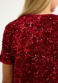 Rød paliet-top med en struktureret overflade, der har en afslappet pasform og korte ærmer, hvilket skaber et livligt og reflekterende udseende.