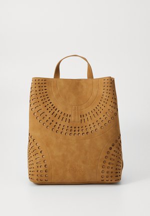 Sac à dos en faux cuir tan avec des motifs circulaires découpés, une poignée supérieure et une texture lisse. Présente un logo près de la base.