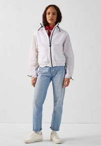 Witte lichtgewicht jas met zwarte rits en een trekkoordcapuchon, gecombineerd met lichtblauwe jeans en witte sneakers. Soepele textuur, casual pasvorm.