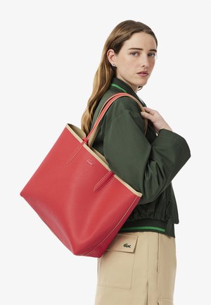 Borsa a tote rossa con texture, rifinita con bordi e manici beige, caratterizzata da un design minimalista e un sottile dettaglio del logo.