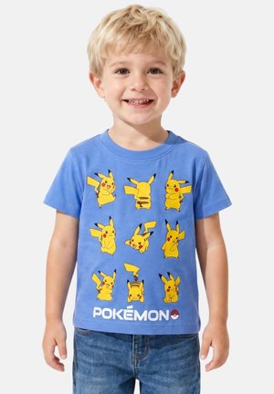 Jeune garçon souriant, portant un T-shirt bleu avec neuf personnages Pikachu dans différentes poses et le texte « Pokémon » en dessous.